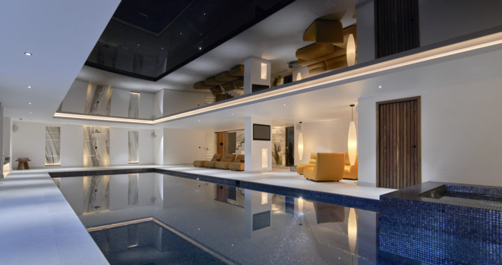 A contemporary indoor swimming pool with a transparent glass wall, allowing natural light to illuminate the space.
